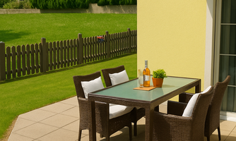 A terrace with a modern table and chairs made of rattan. In the background, green meadows and trees can be seen.