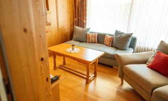 A cozy living area with wood paneling, a table, and two sofas. Plenty of daylight flows through the windows, which are decorated with curtains.