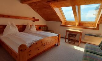 A cozy room with two wooden beds and a wooden ceiling. The room has large windows that let in plenty of daylight.