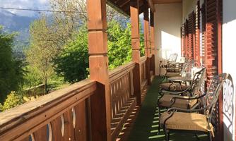 A beautiful balcony with a wooden railing and several chairs. The surroundings are green and the sun is shining.