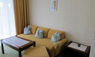 A cozy living room with a yellow sofa and cushions. The room has a bright, friendly look with a coffee table and a small side table.