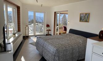 A bright bedroom with a large bed and a view of the mountains.  
Large windows let in plenty of light and create an inviting atmosphere.