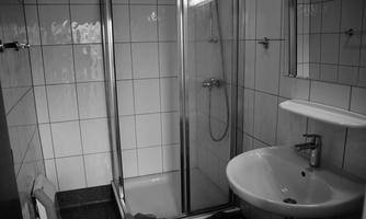 A modern bathroom with a shower and a sink. The walls are tiled with white tiles and the floor is dark.