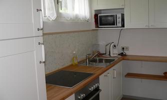 A modern kitchen with white cabinets and wood countertops. It is equipped with a stove, a sink, and a microwave.