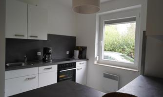 A modern kitchen with white cabinets and a dark countertop. The view from the window shows green trees outside.