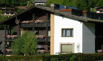 A modern building in a green landscape. It has balconies with flowers and a clear, sunny atmosphere.