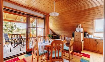 A cozy dining area with wooden chairs and a table. Large windows offer a view of a terrace with garden furniture.