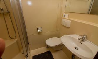 A small bathroom with a shower, toilet, and washbasin. The walls are painted in a light color.