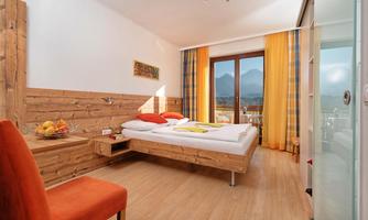 A modern bedroom with wooden details and large windows. The room is cozily furnished and offers a view of the mountains.