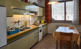 A bright kitchen with modern appliances and a dining table. The windows let in plenty of daylight.