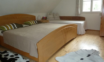 A cozy bedroom with a large bed and a single bed. The floor is made of wood, and a cowhide is on the floor.