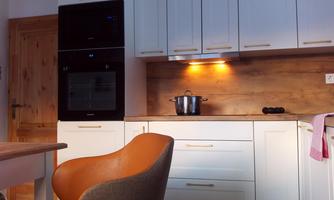 A modern kitchen with white cabinets and wooden paneling. A chair and a pot on the stove are visible.