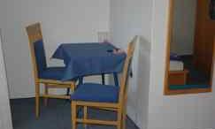 A simple table with a blue tablecloth and two chairs stands in a room. In the background, a mirror is visible.