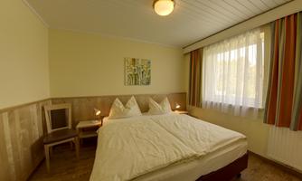 A cozy bedroom with a large bed and bright curtains. The room has a warm atmosphere and a beautiful wall mural.