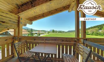 A cozy balcony with wooden furniture and a view of a green landscape. The sky is clear and the surroundings are quiet.