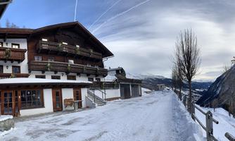 A picturesque chalet in the snow, surrounded by a wintry landscape. The sky is overcast and the road is covered in snow.