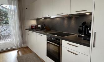 A modern kitchen with white cabinets and a dark work area. It is well-equipped with a stove, an oven, and kitchen utensils.