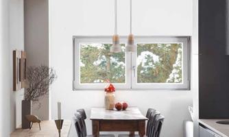 A bright and modern dining room with a wooden table and black chairs. Large windows let in plenty of light and offer a view of trees.