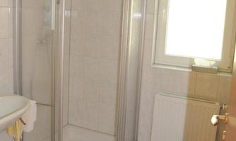 A bathroom with a glass shower cabin and white towels. Light streams through a window and the walls are brightly tiled.