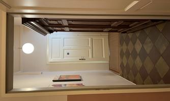 A hallway with a stylish wooden cabinet and a white front door in the background. The walls are painted in soft colors and the floor tiles are patterned.