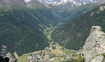 An impressive mountain landscape with snow-covered peaks and a picturesque valley. In the valley lies a small village surrounded by lush nature.