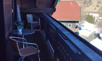 A balcony with two chairs and a small table. In the background, snow-covered landscapes and houses can be seen.