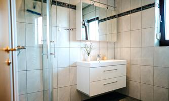 A modern bathroom with white tiles and an elegant sink. The large mirror reflects the light and creates a bright atmosphere.