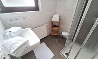 A modern bathroom with a shower and a sink. Clean towels are ready, and there is a small stool as well as a towel rack.