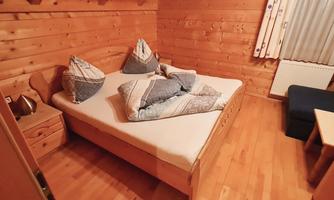 A cozy room with wooden walls and a double bed. Decorative pillows are on the bed and a couch is in the corner.