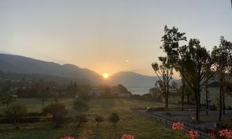 A beautiful sunrise over the mountains and the lake. In the foreground, flowers are blooming, complementing the serene landscape.