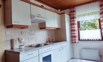 A modern kitchen with white cabinets and a wooden ceiling. On the wall are windows with curtains and the same view of nature.