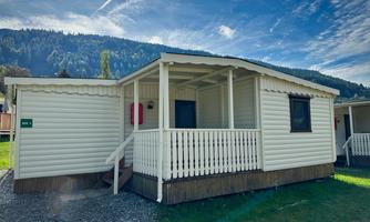 A cozy mobile home with a porch. In the background, there are green mountains and a blue sky visible.