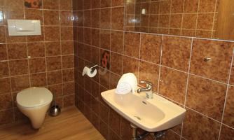 A bathroom with brown tiles and wooden floors. There is a sink, a toilet, and fresh towels.