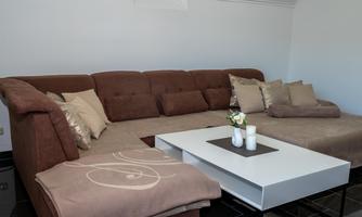 A modern living room with a brown sofa and cushions. A white table with decorative elements is in the center of the room.