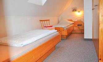 A simple bedroom with two wooden single beds. The walls are bright and the light is warm and inviting.