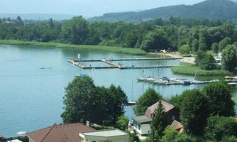 A calm lake landscape with boat docks and green shores. In the background, gentle hills and forests can be seen.