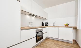 A modern kitchen with white cabinets and a wooden worktop. The equipment includes a stove, a coffee machine, and a fruit bowl.