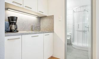 A small kitchen corner with a coffee machine and bright cabinets. In the background, a shower is visible.