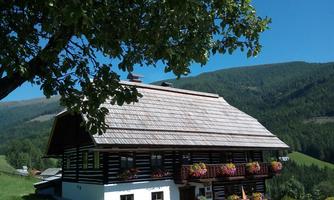 A traditional, multi-story wooden house with colorful flowers in front of the window. In the background, green hills and a clear blue sky can be seen.