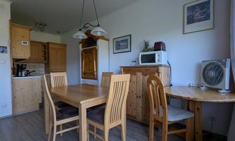 A cozy kitchen with wooden furniture and a dining table. The amenities include ovens, a refrigerator, and a microwave.