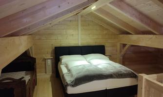 A cozy bedroom in the attic with wooden paneling. The bed is modern and inviting, surrounded by a warm atmosphere.