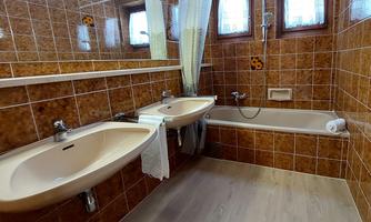 A bathroom with two sinks and a bathtub. The walls are tiled with brown tiles.