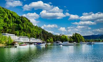 A beautiful lake with sailboats and surrounding green hills. The sky is clear with some clouds.