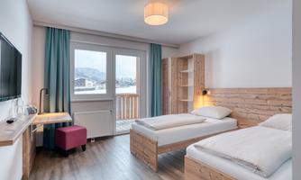 A modern hotel room with two single beds. The room features large windows with a view of the mountains and is bright and invitingly furnished.