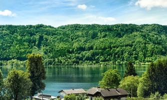 A tranquil lake surrounded by green hills and trees. In the foreground, some houses are visible, embraced by nature.