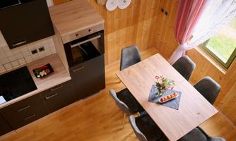 A modern kitchen with wooden shelves and a dining area. The table is lovingly set and decorated with fresh flowers.