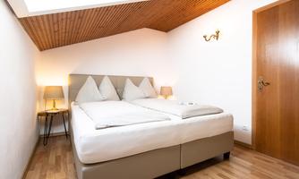 A cozy bedroom with a double bed and soft pillows. The walls are bright and the wooden floor contributes to the pleasant atmosphere.