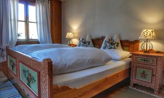A cozy bedroom with a wooden bed and decorative cushions. Two nightstands with lamps and a window that allows daylight to enter.