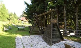 A beautiful outdoor playground with a swing and a slide. Surrounded by trees and a green meadow.
