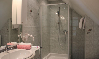 A modern bathroom with a shower and sink. The walls are brightly tiled, and towels and cosmetics are visible.
